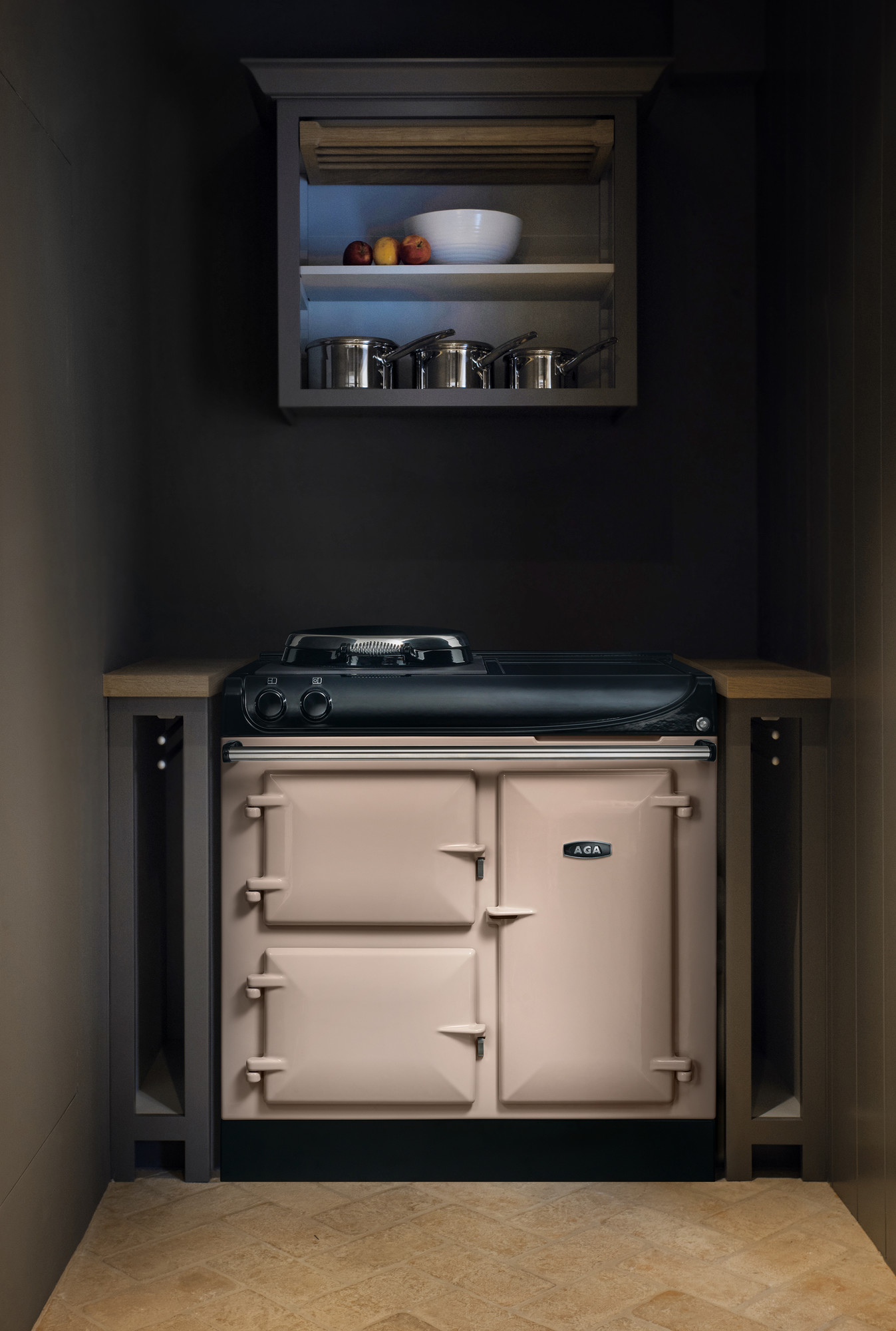 Stylischer, beiger AGA Herd in einer kleinen modernen Küche unter einem Hängeschrank mit Edelstahltöpfen, Schale und Äpfeln