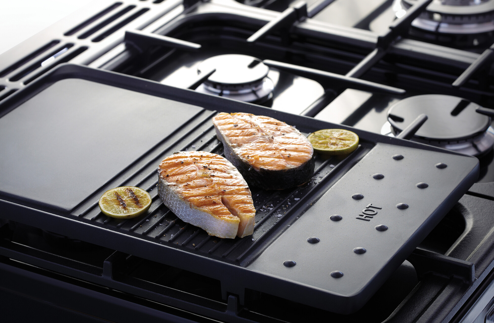 Zwei Lachssteaks und Limettenscheiben werden auf einer Grillplatte auf einem Gasherd zubereitet